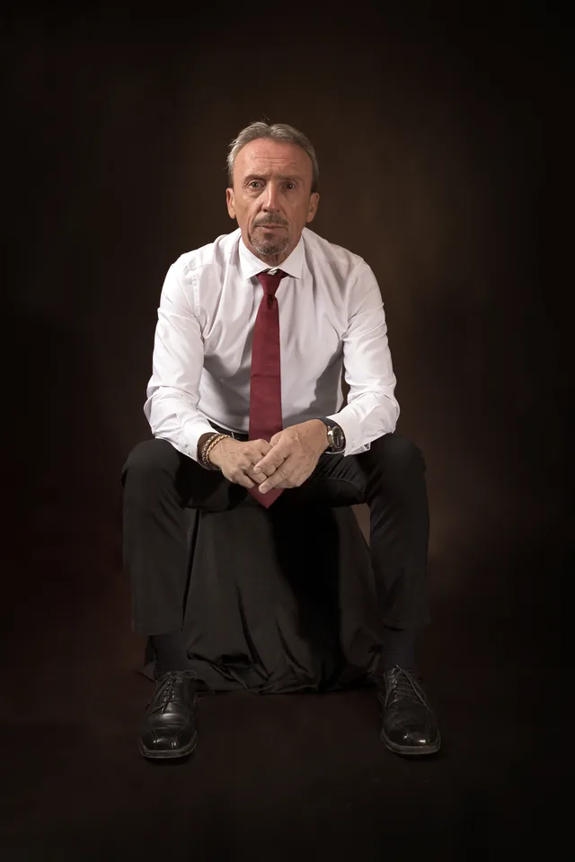Paco Gumiel sentado, con camisa blanca y corbata granate, sobre fondo oscuro